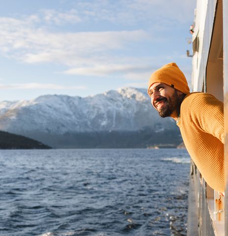 Ein lächelnder Mann lehnt sich aus einem Schiff und bewundert die wunderschöne verschneite Berglandschaft