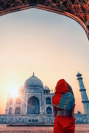 Frau im roten Sari blickt durch einen Torbogen auf das Taj Mahal in Agra, Indien