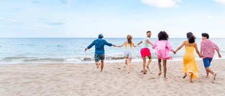 Gruppe junger Leute läuft Hand in Hand am Strand Richtung Meer