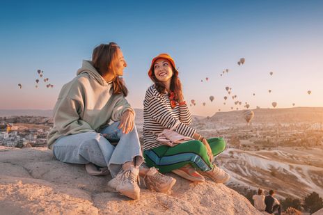 Frauen sitzen auf einem Felsen in Kappadokien und genießen den Ausblick auf die Heißluftballons