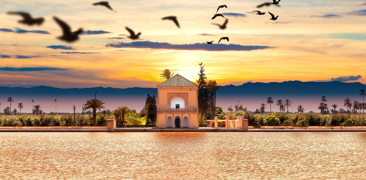 Menera Garten in Marrakesch in Marokko bei Sonnenuntergang mit Vögeln über dem Haupthaus