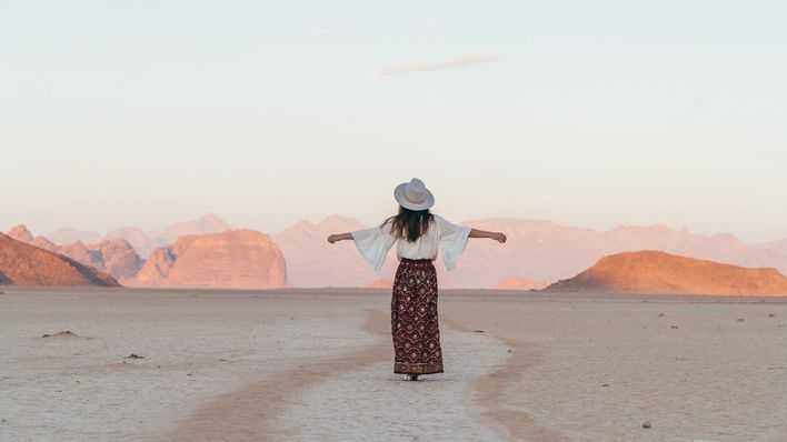 Frau mit ausgebreiteten Armen und Hut in einer Wüste in Jordanien mit Felsen im Hintergrund