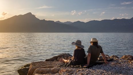 Paar sitzt am Ufer des Gardasees und genießt den Sonnenuntergang mit Blick auf die Berge