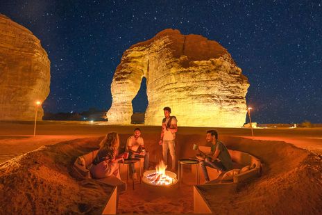 Wüstenlager bei Nacht mit Feuerstelle und beleuchteten Felsen in Saudi-Arabien