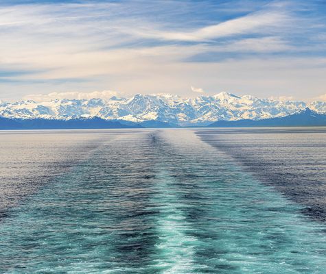 Blick auf die Fahrspur eines Kreuzfahrtschiffs im Prince William Sound mit schneebedeckter Bergkulisse in Alaska