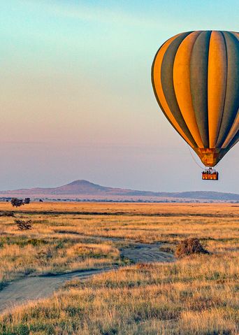 Heißluftballon fliegt bei Sonnenaufgang über den Serengeti Nationalpark in Tansania